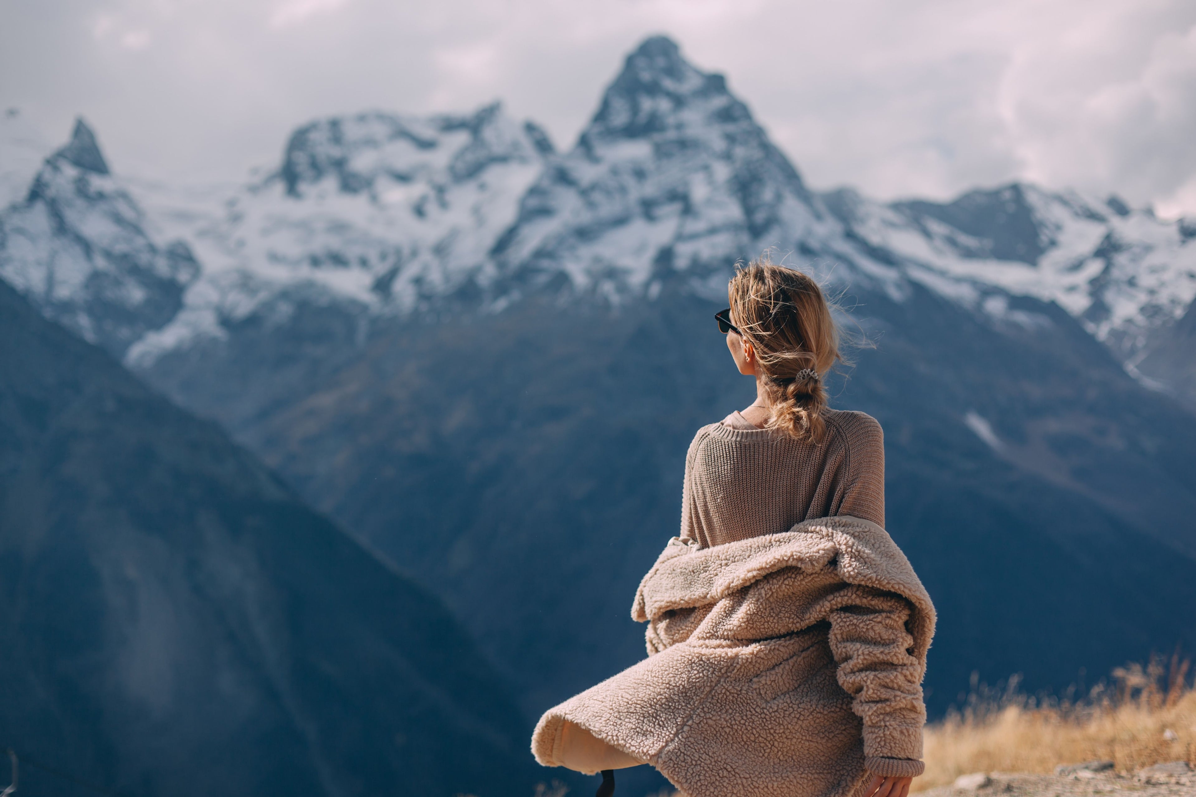 Person standing on a cliffside with a scenic view of mountains in the background